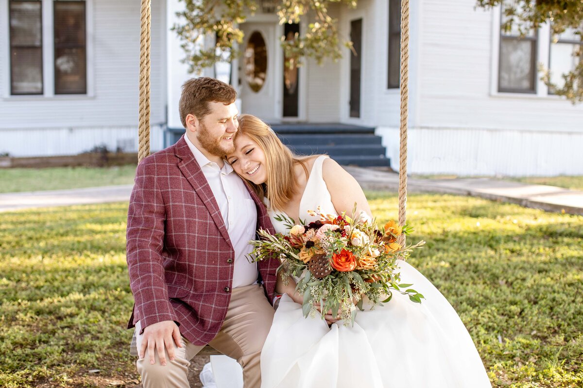 bride lays head on shoulder of groom while sitting on swing at Allen Farmhaus  in New Braunfels Texas