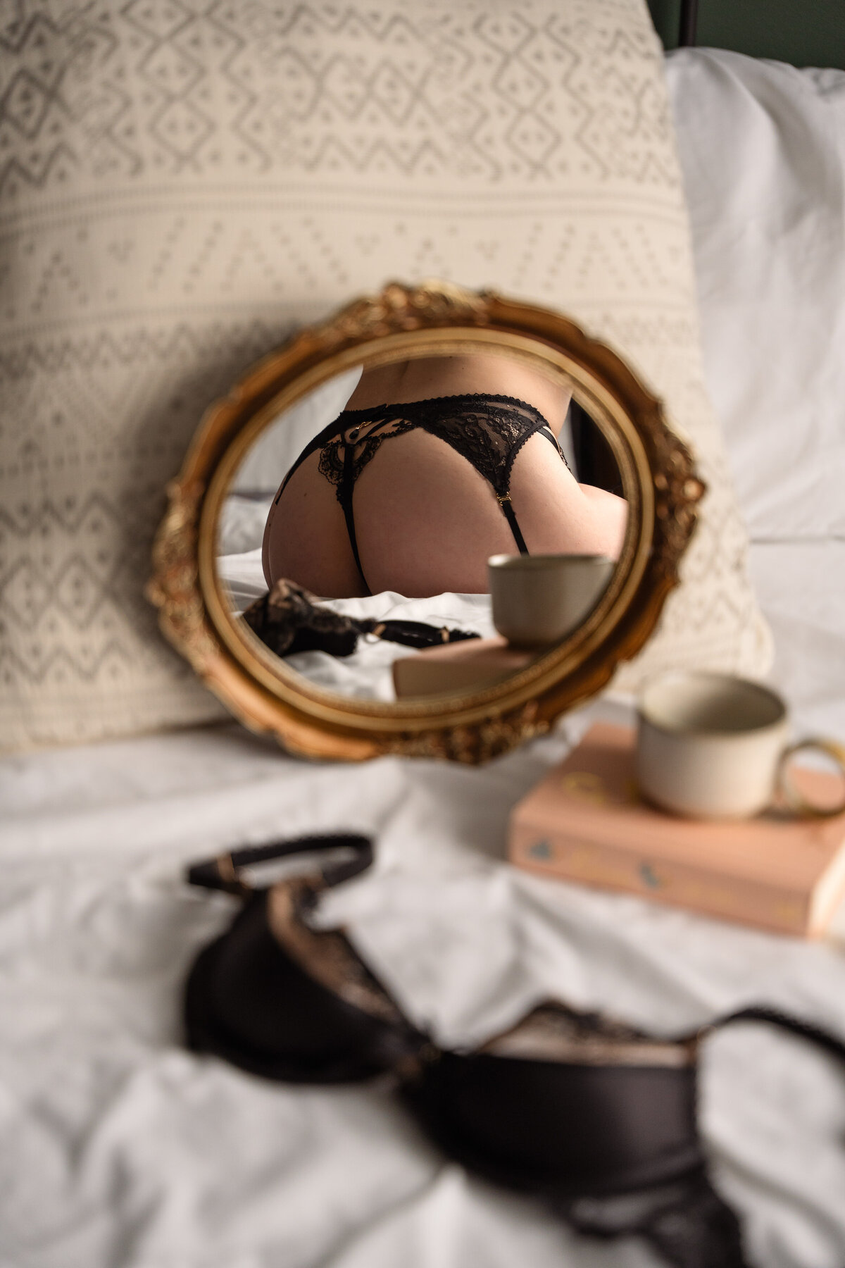 bra, book and coffee on a bed with a mirror showing the reflection of a butt