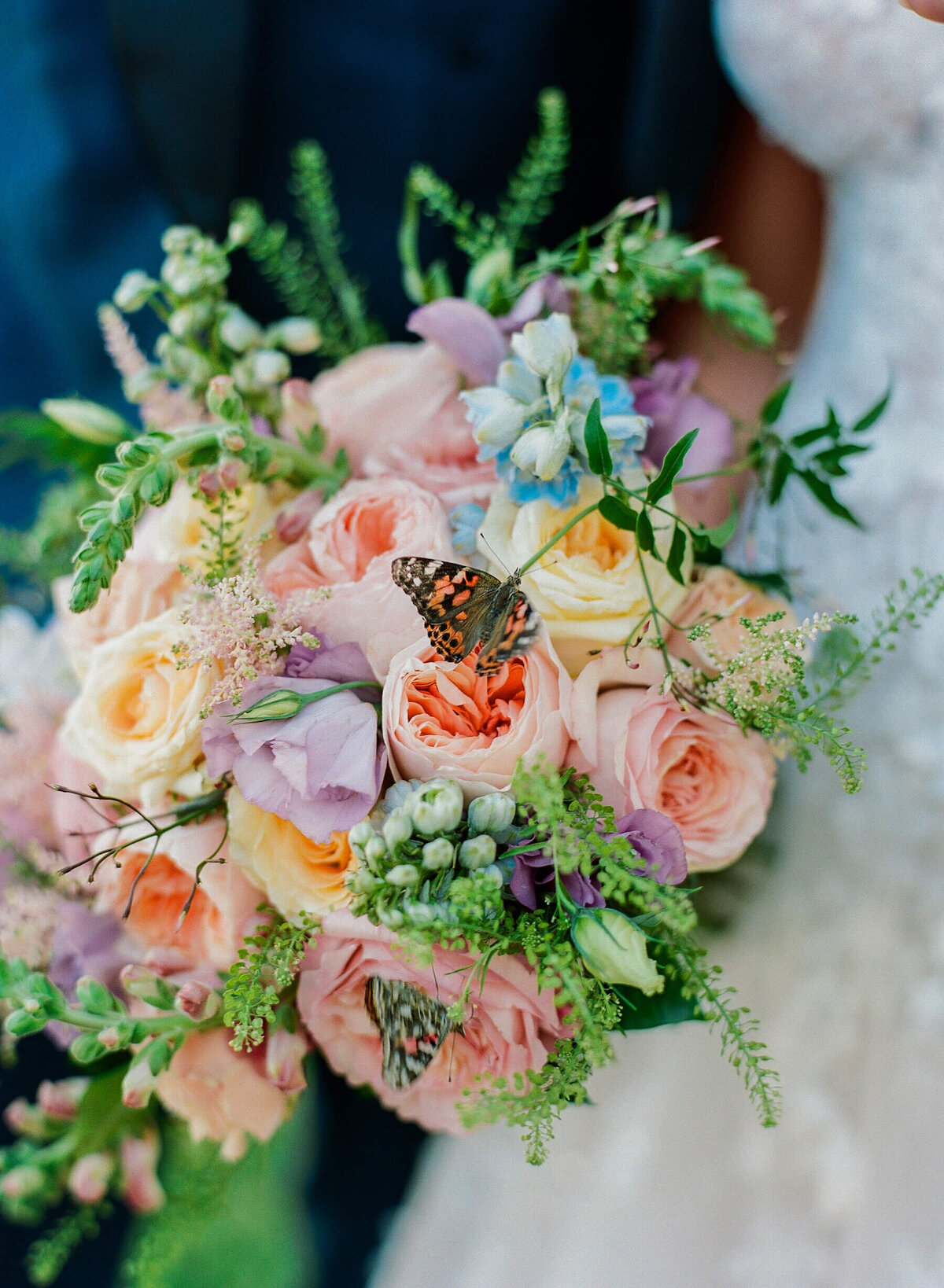 Peach, purple, green, yellow bridal bouquet with roses, berries and live butterflies.