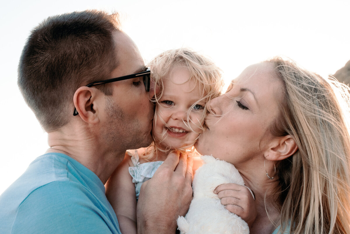 Mom and Dad kiss toddler girl for family photo