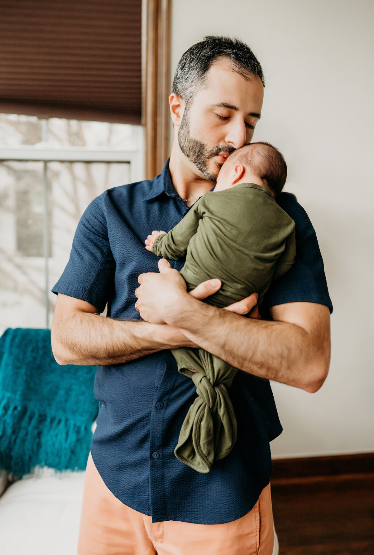 Newborn Photographer, a father tenderly leans into his baby son's head as he holds him