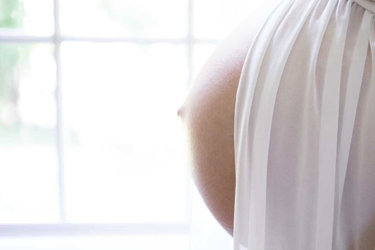 Detail shot of a pregnant belly in framed by white fabric Hudson Valley maternity photographer Milestone Images