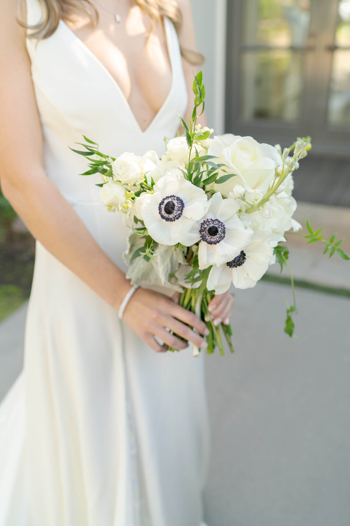 Bride in an elegant sleeveless  white wedding dress holding a bouquet of black-eyed anemones.