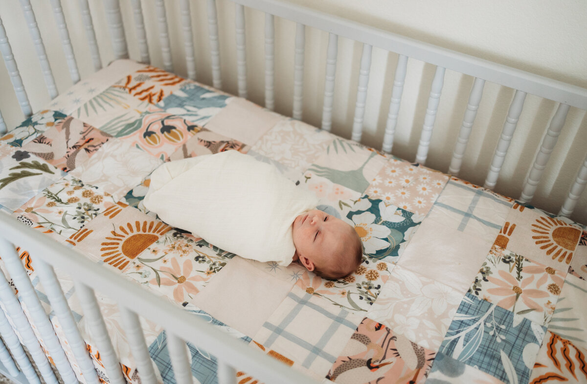 newborn baby girl lays in crib wrapped in white blanket  on  homemeade quilt
