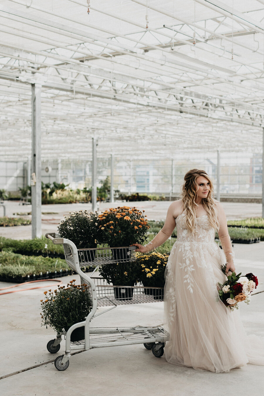 Bride in her wedding dress with her bouquet and a shopping cart of flowers.