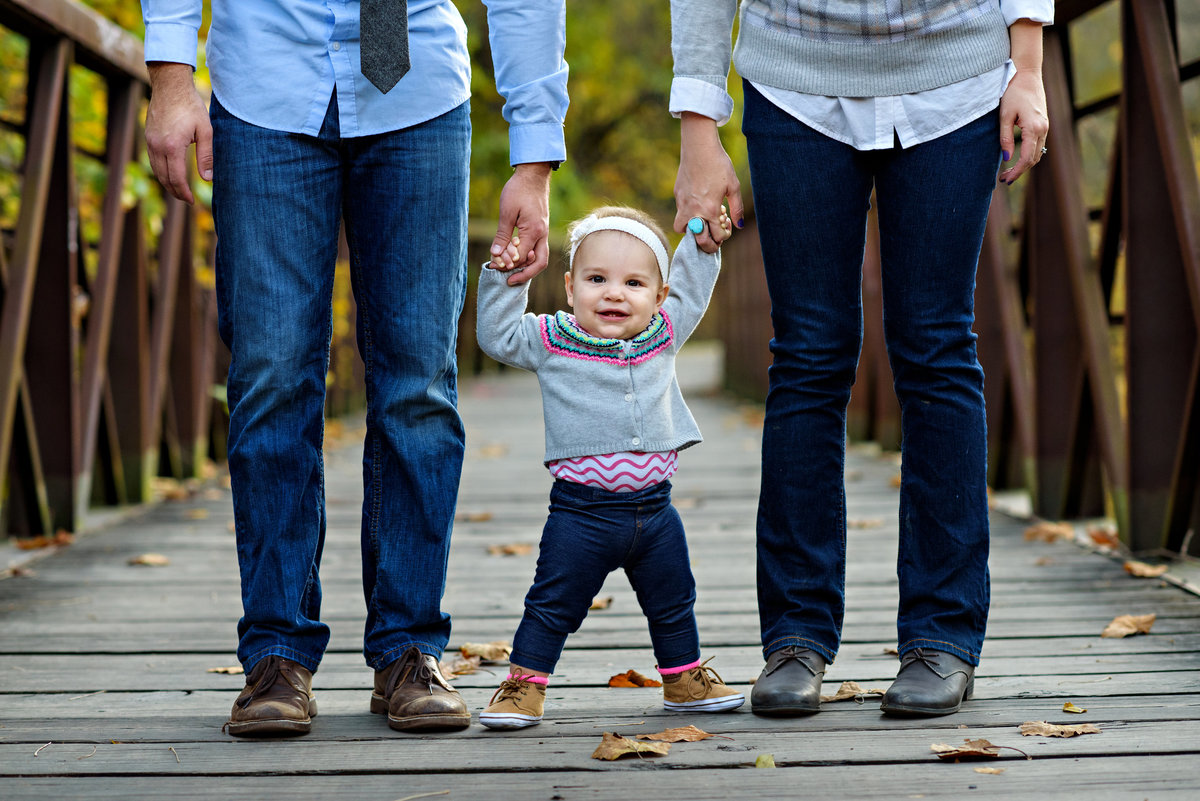 A baby walks with the help of her parents on the bridge in a philadelphia park.
