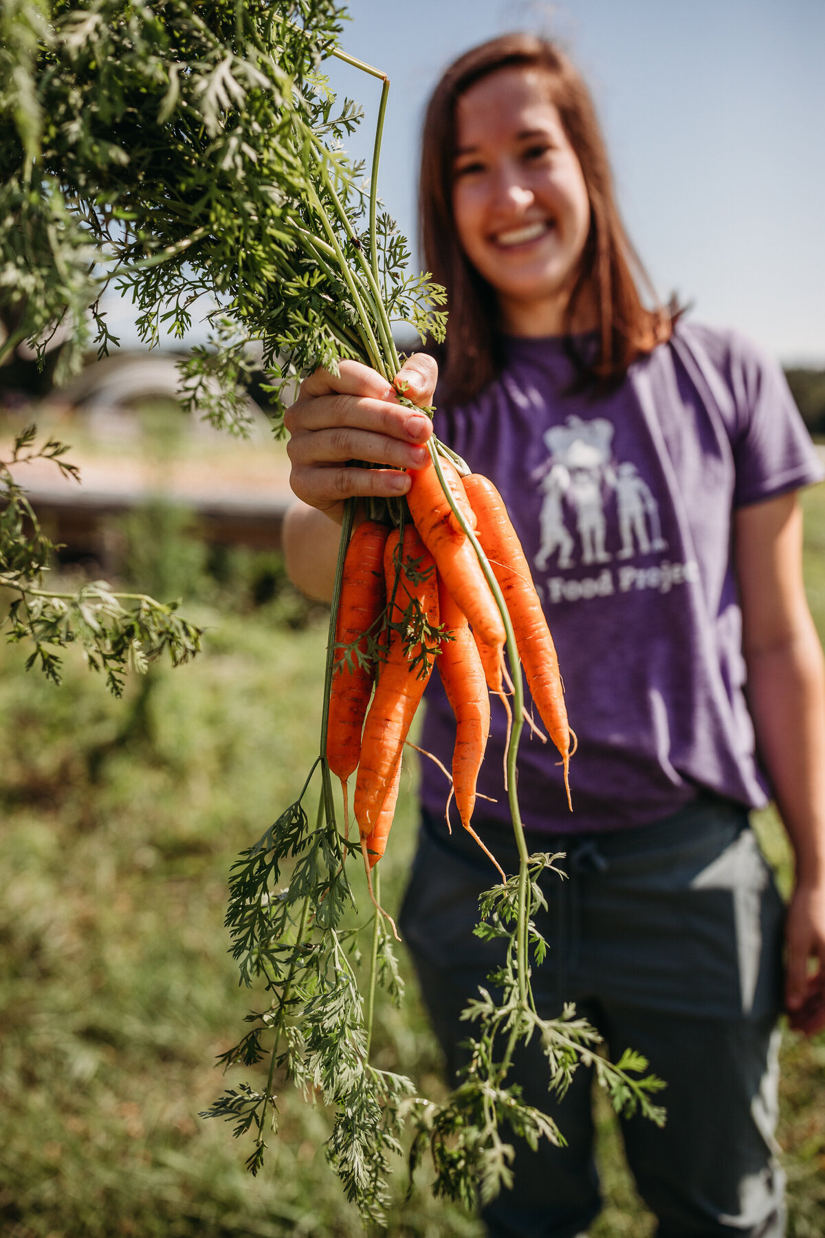 farmer holds buch of carrots toward camera