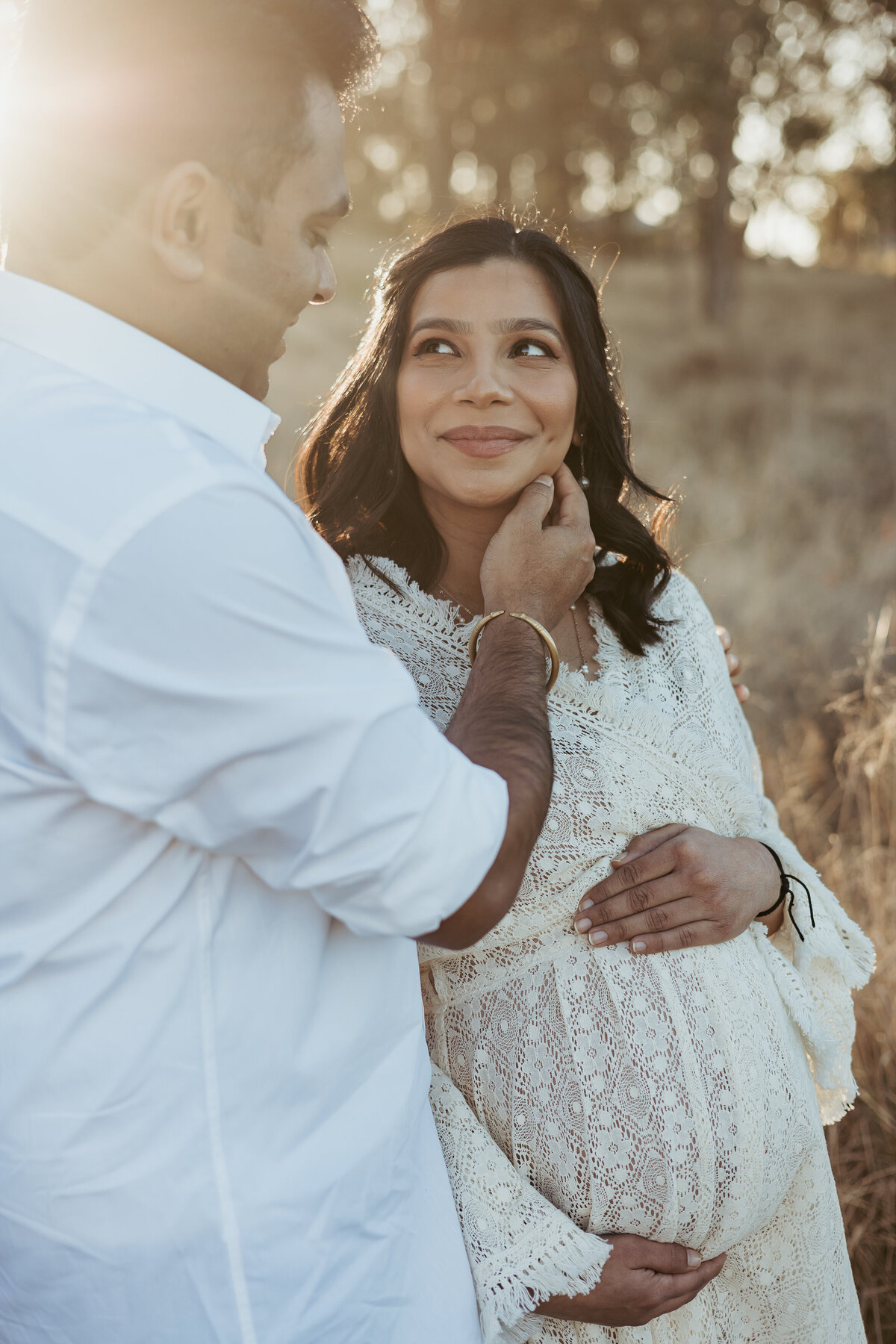 Dad-to-be casually grazing his wife's cheek  while she looks up at him and holds her baby bump