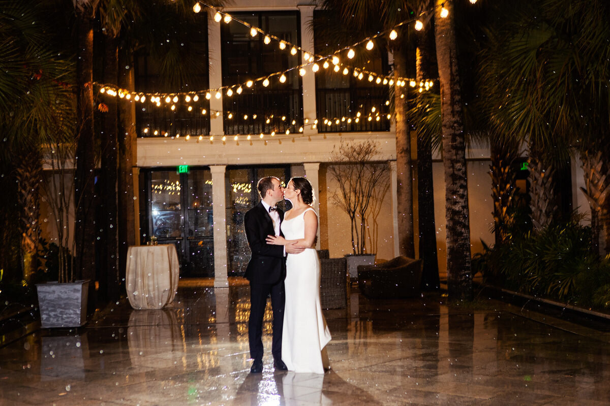 Charleston Wedding Photographer Bride and groom kiss in the rain under string lights at Cannon Green