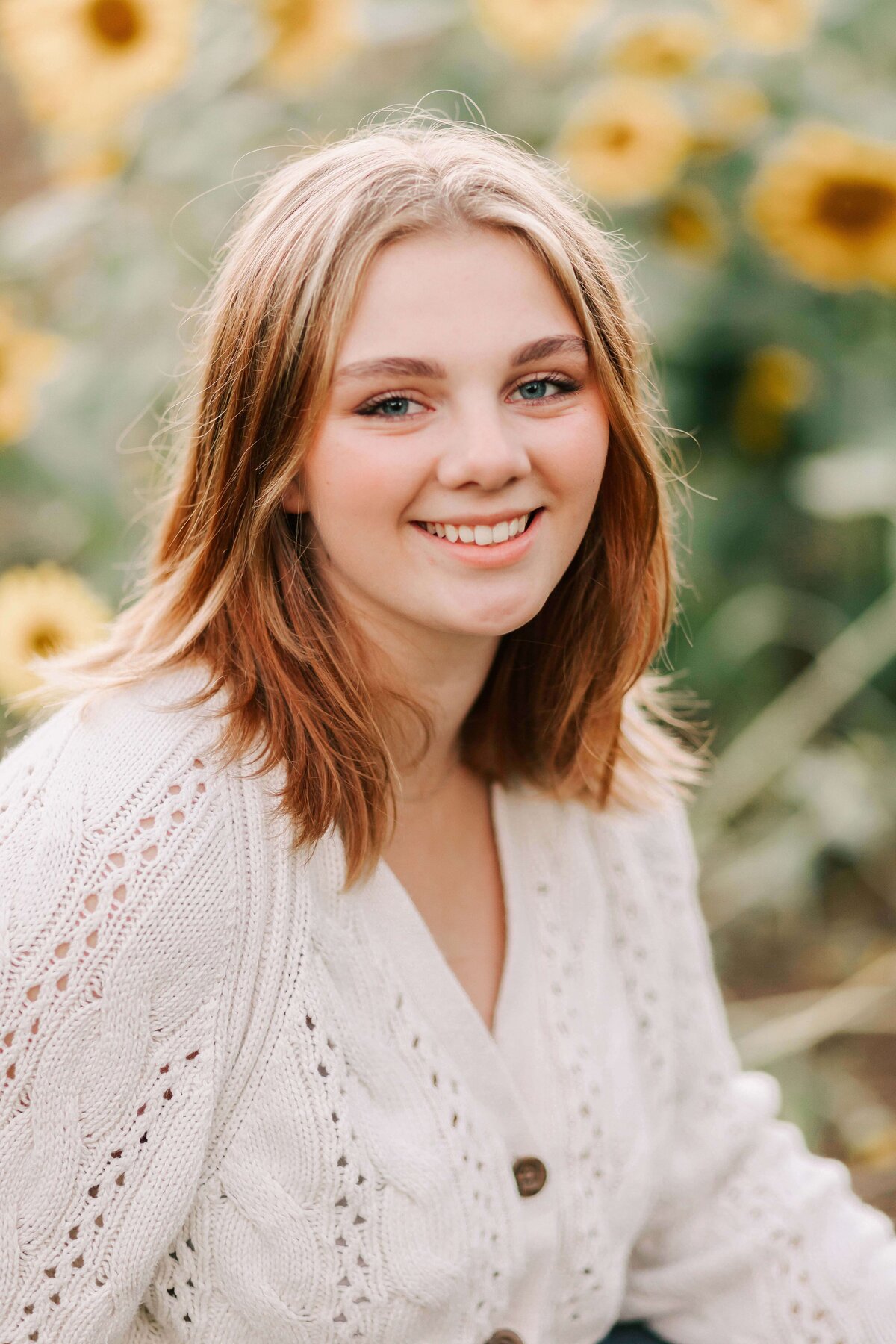 A girl in a white sweater sits in a sunflower field