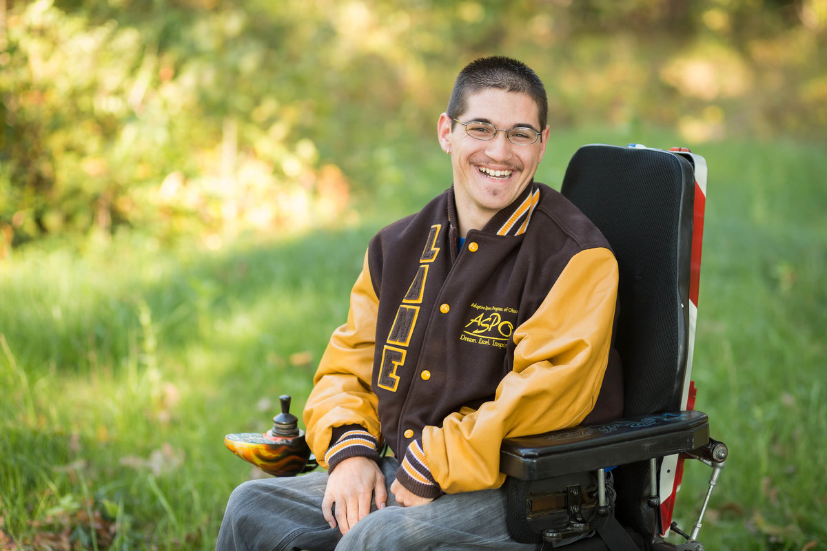 waynedale high school guy in a wheelchair wearing his letterman jacket looking at camera with big smile, photographed by Jamie Lynette Photography Canton Ohio Senior Photographer