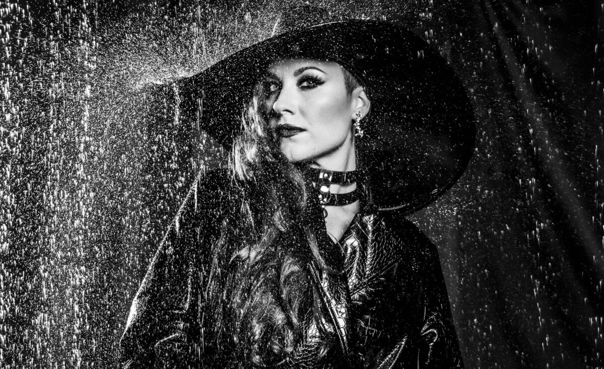Female musician portrait Tarra Layne  black and white wearing black hat black overcoat rain pouring down