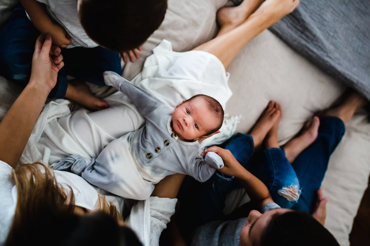 newborn lifestyle session, DFW, baby looking up at camera with family surronding him