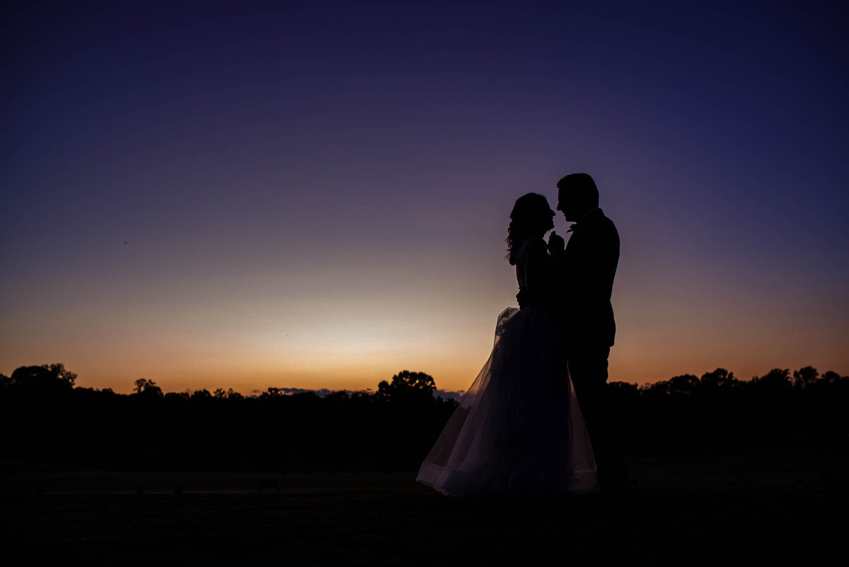 Purple-and-orange-sunset-silhouette-of-a-groom-tipping-his-bride's-chin-as-he-leans-in-for-a-kiss-at-Pine-Island-Country-Club