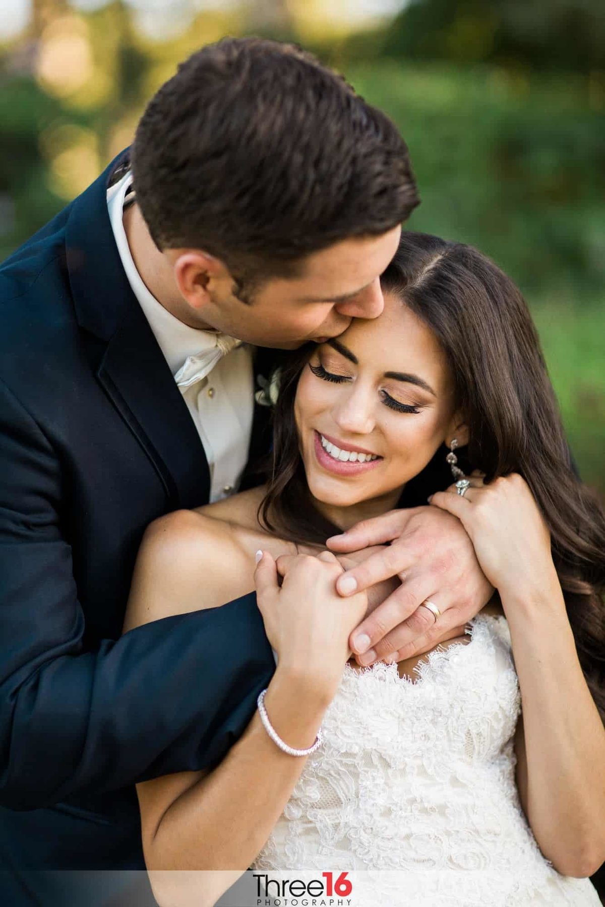 Groom fully embraces his Bride from behind and kisses her forehead leaving the Bride with a huge smile on her face