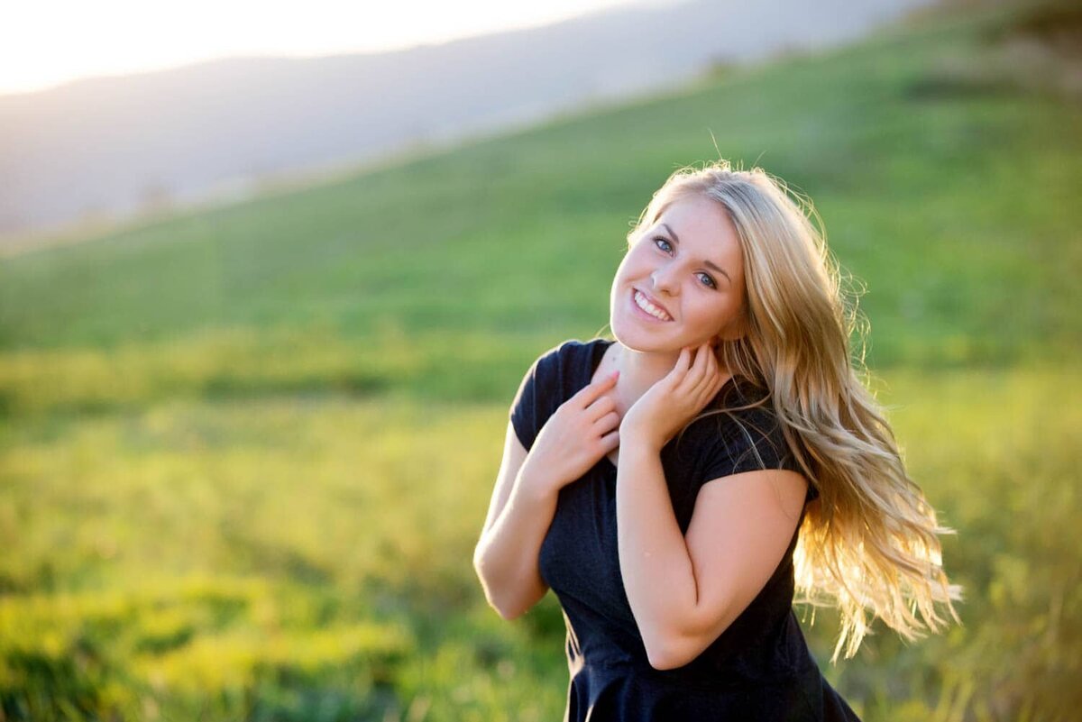 Colorful senior photo of girl in grass field and wind blowing through her hair.