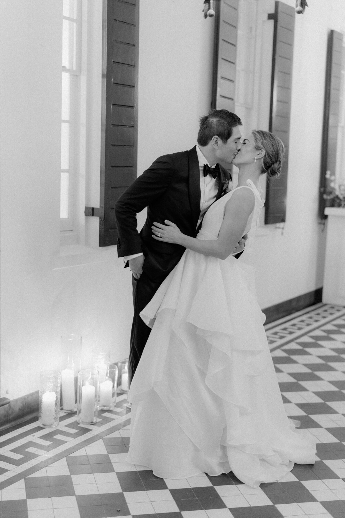 Spring Lowndes Grove wedding. Bride and groom kiss on checkerboard floor. Black and white wedding photo. Kailee DiMeglio Photography.