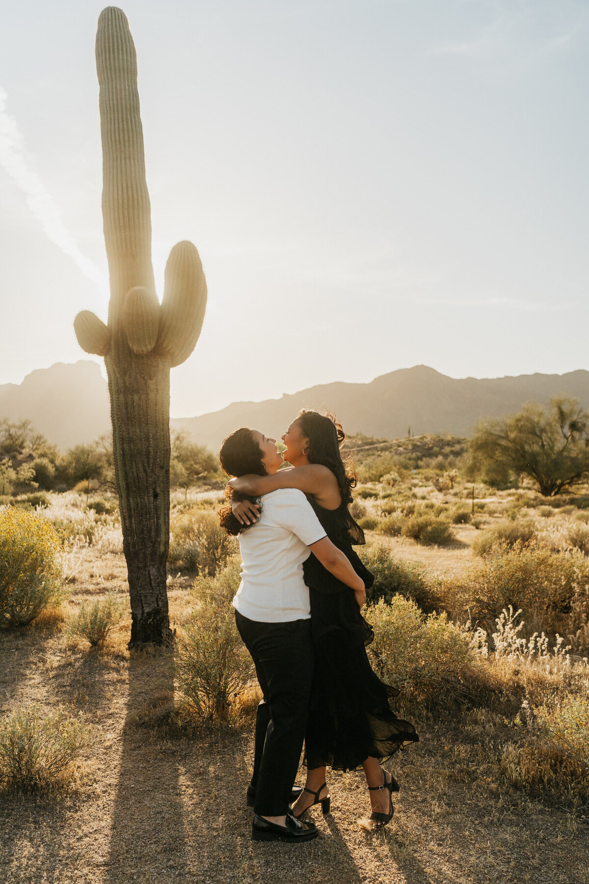 A couple hugging and laughing in front of a cactus 