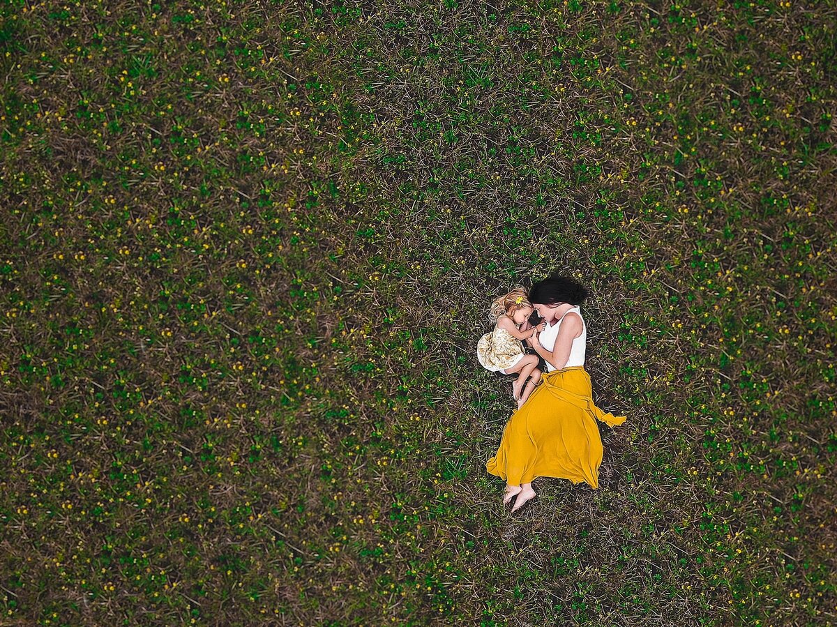 drone image of mother and daughter in yellow dresses in field of grass with yellow flowers