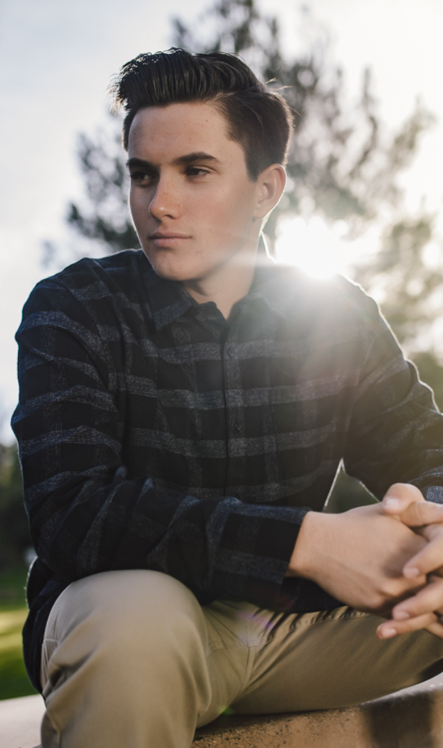 boy in a plaid shirt looking off to the side with the sun behind him