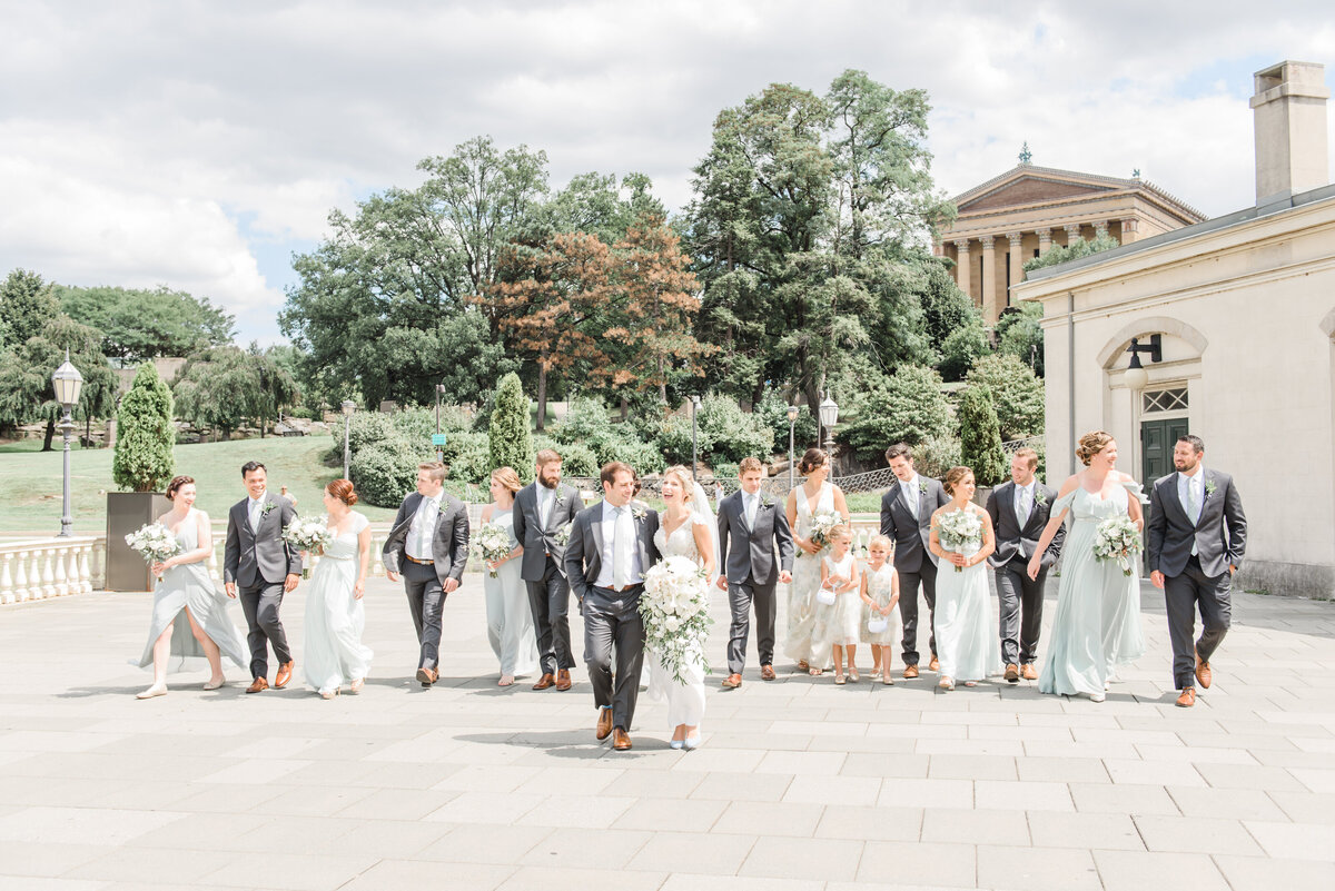 bridal party in light green gowns and dark grey suits walk among the bride and groom