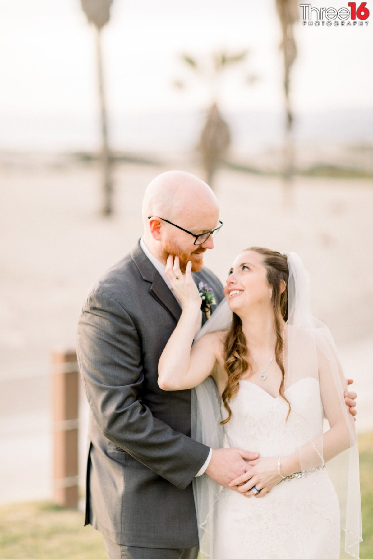 Groom looks down at his Bride as she looks up and smiles while touching his face