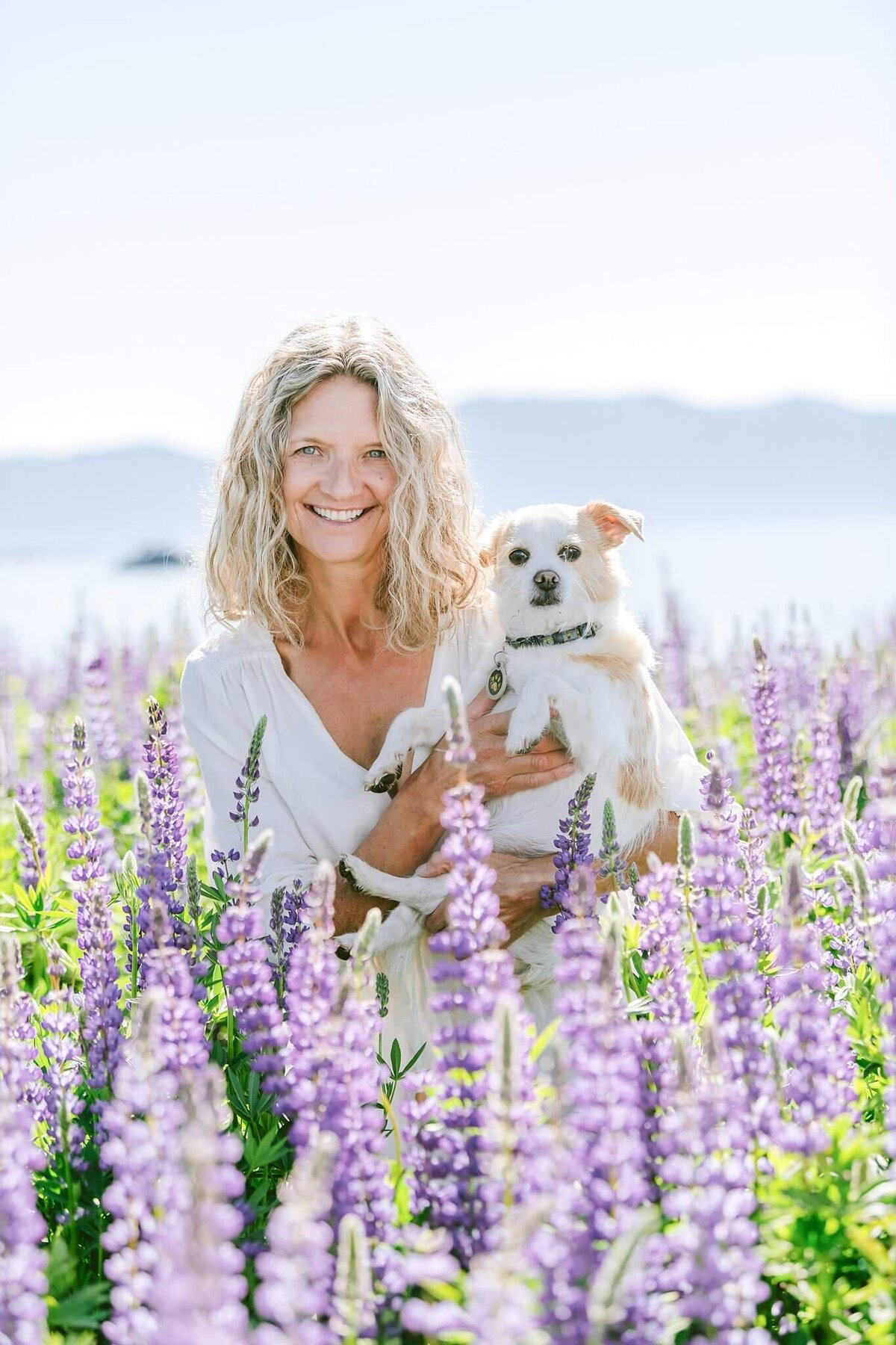 Yoga teacher and activist headshot Sherry McConckey withe her dog in lupines at Lake tahoe