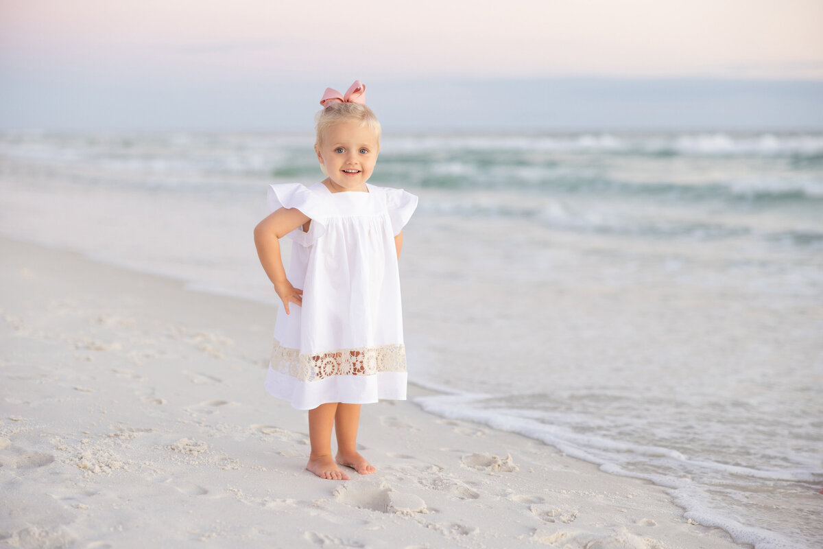 A small girl standing at the beach with her hands on her hips