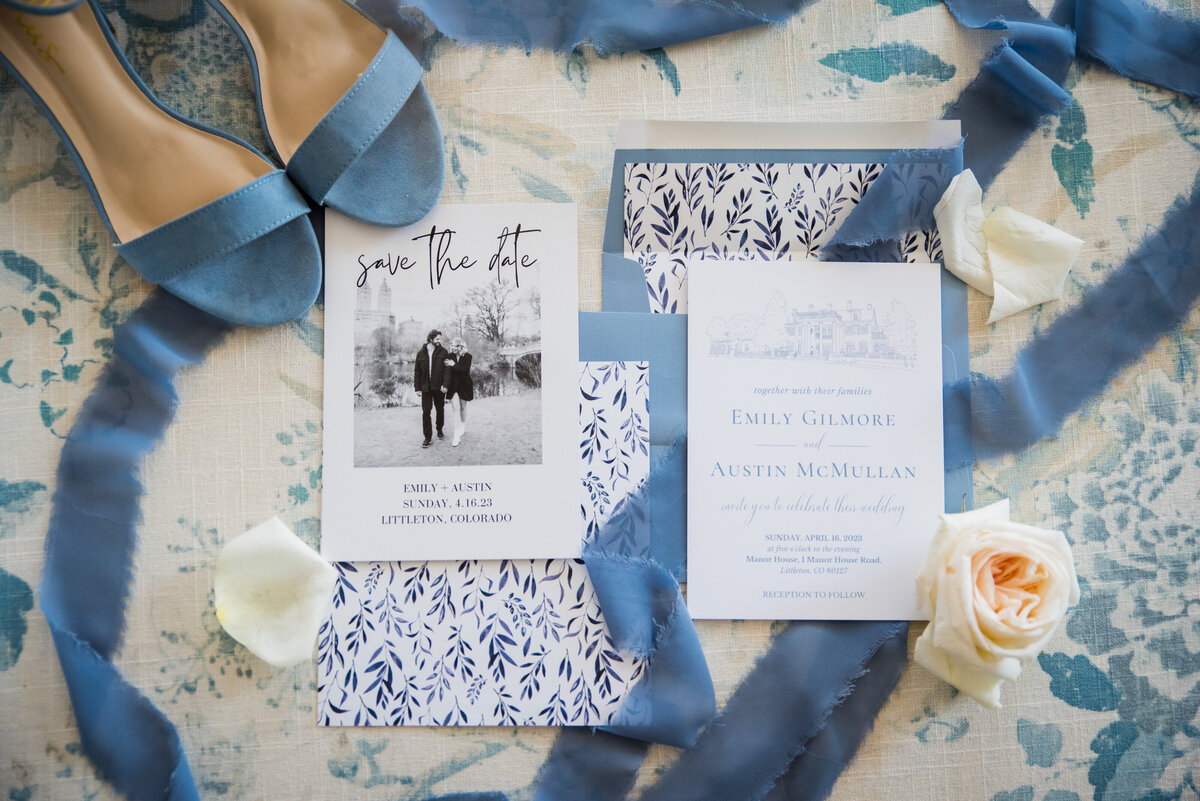 Various wedding details including an invitation suite, accented with blue wedding shoes, blue ribbon, and roses.