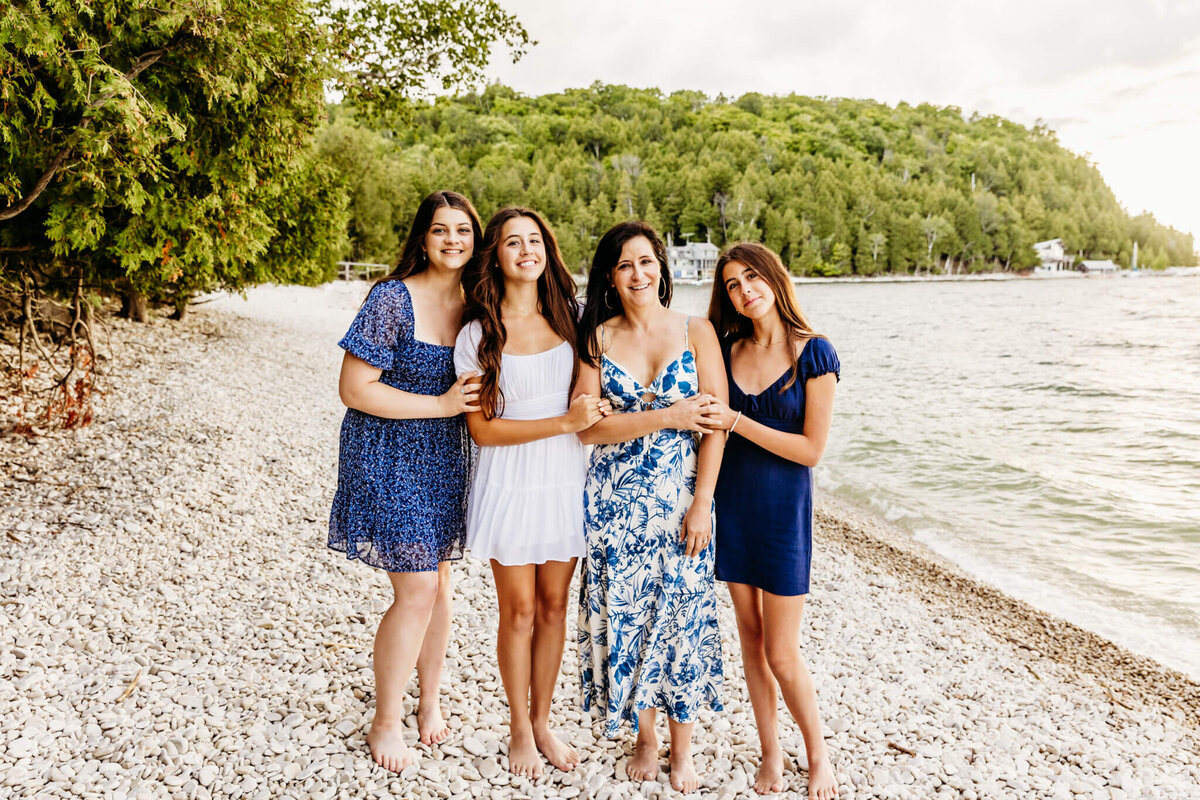 gorgeous mama and her three teen daughters all in blue and white dresses standing on a white pebble beach in door county wisconsin