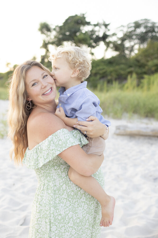 momma in green dress holds son on the beach