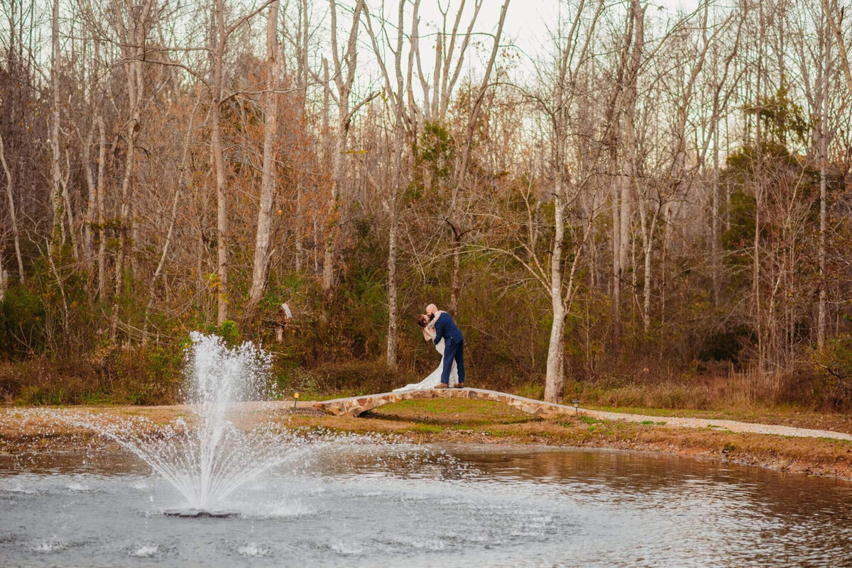 photo of a bride and Groom standing on the far side of a pond and kissing while a fountain sprays