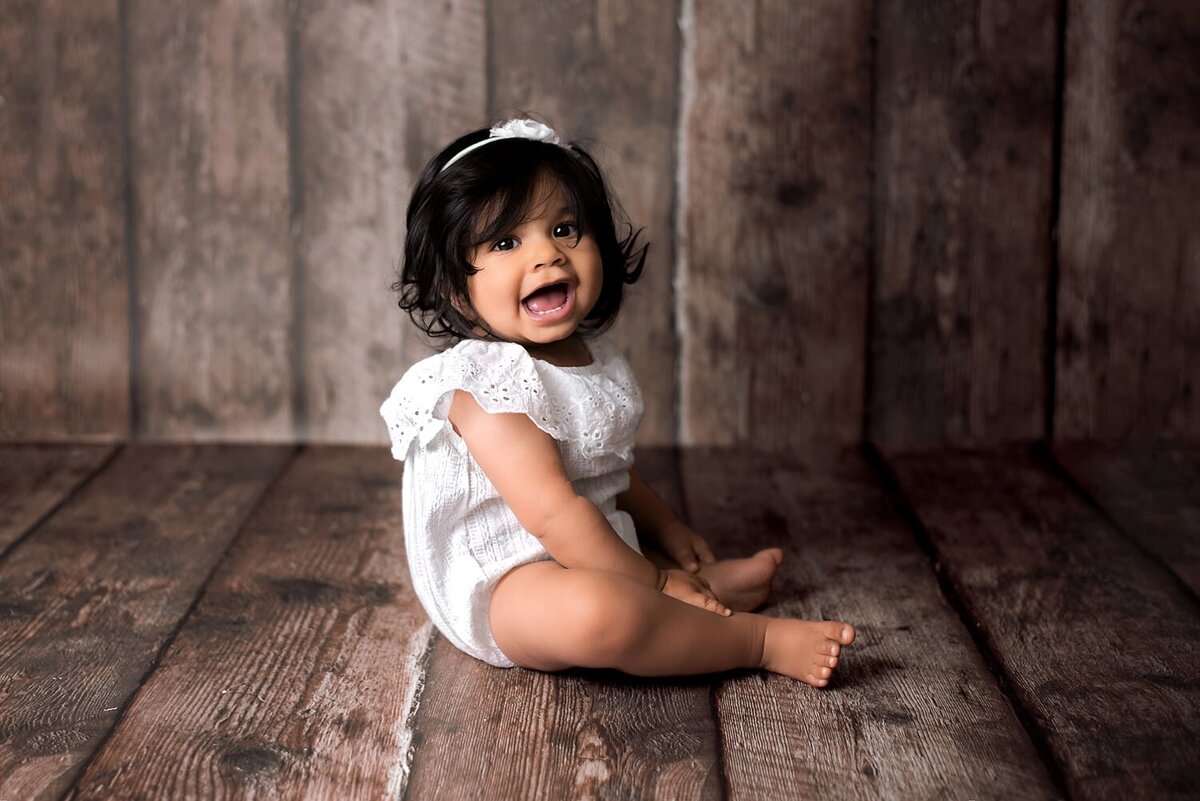 8 month girl in white romper smiling.