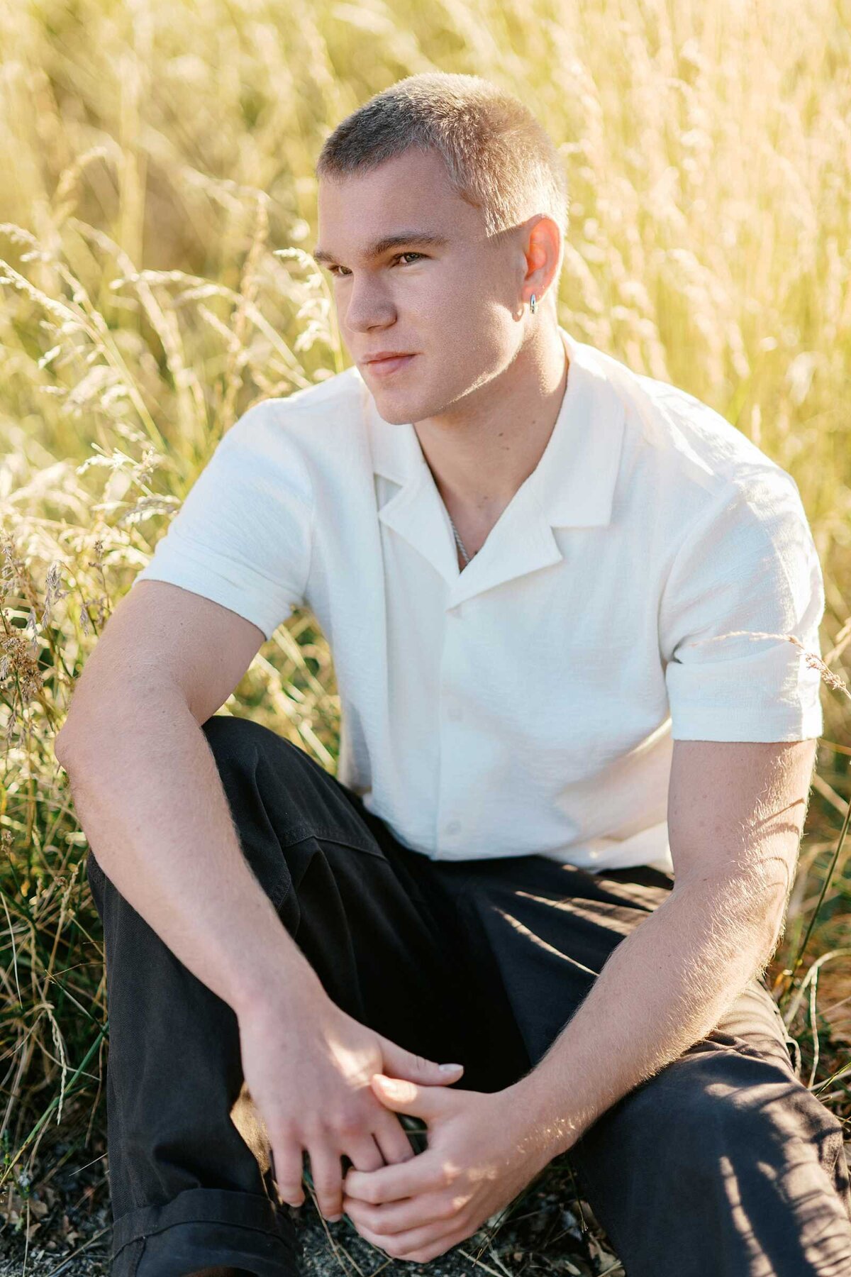 Senior guy picture ideas: a teen boy in a white shirt and black pants seated in a field of grass