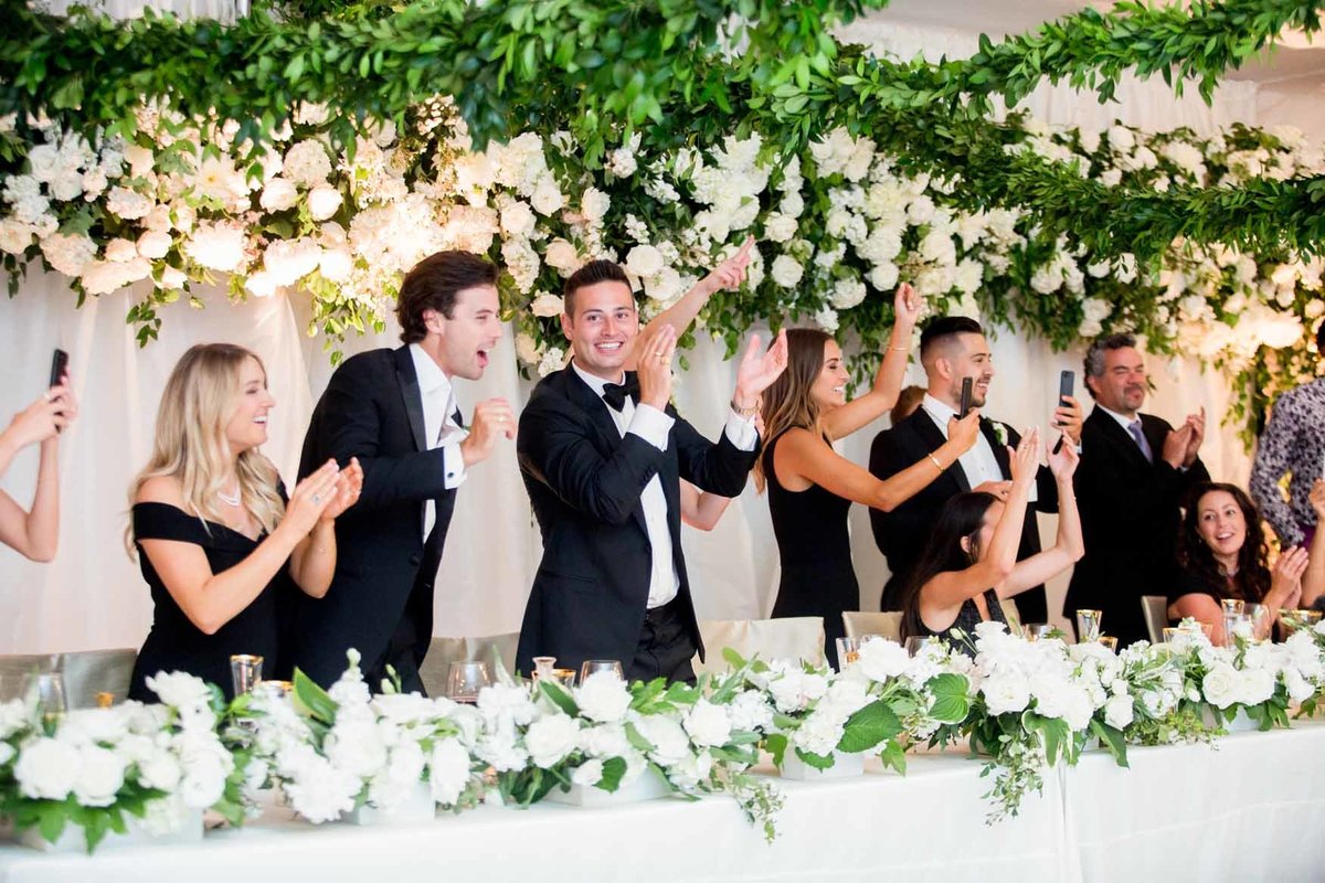 Wedding party behind head table with white floral installation and greenery garlands