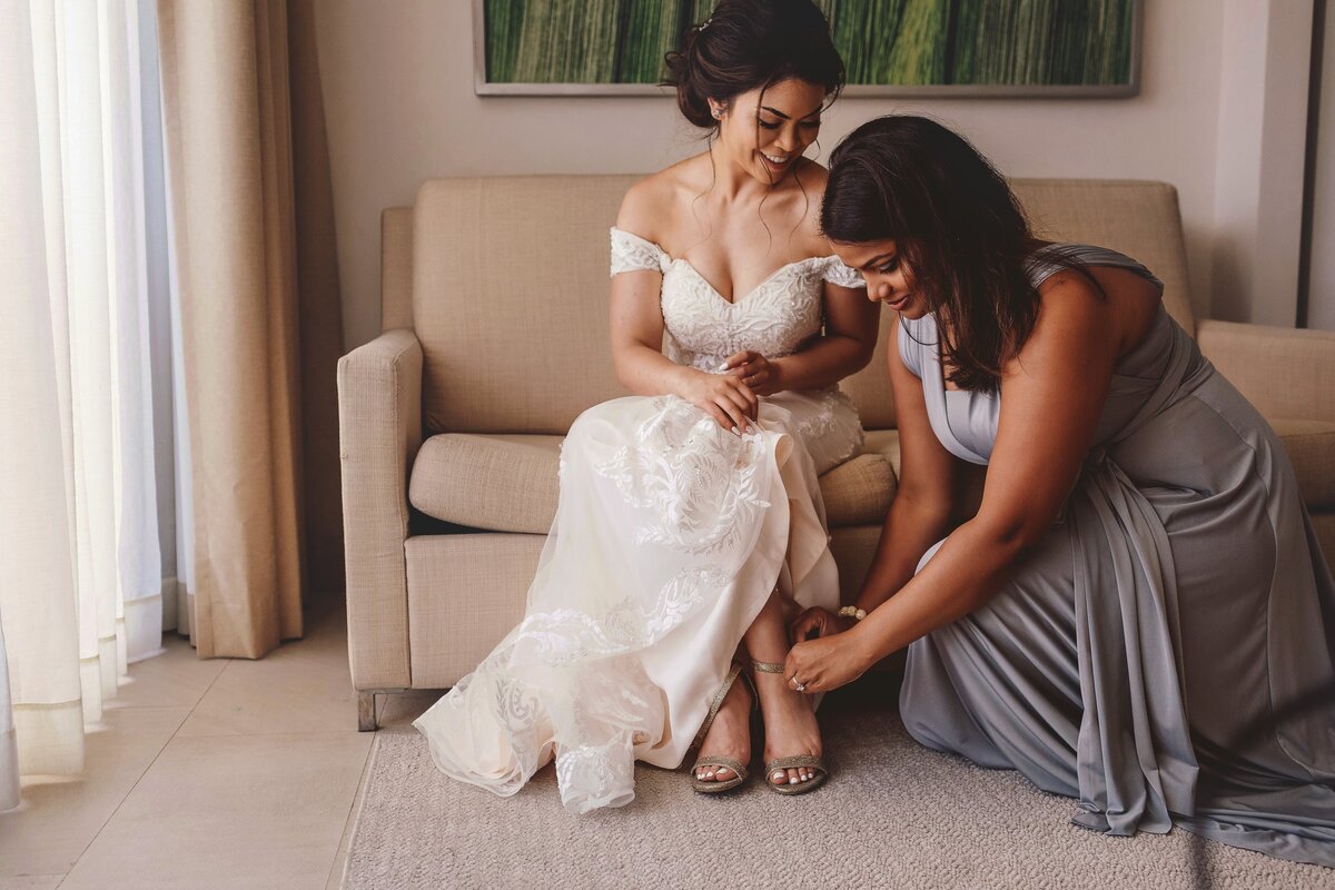 Bridesmaid helping bride with shoes at Cancun wedding