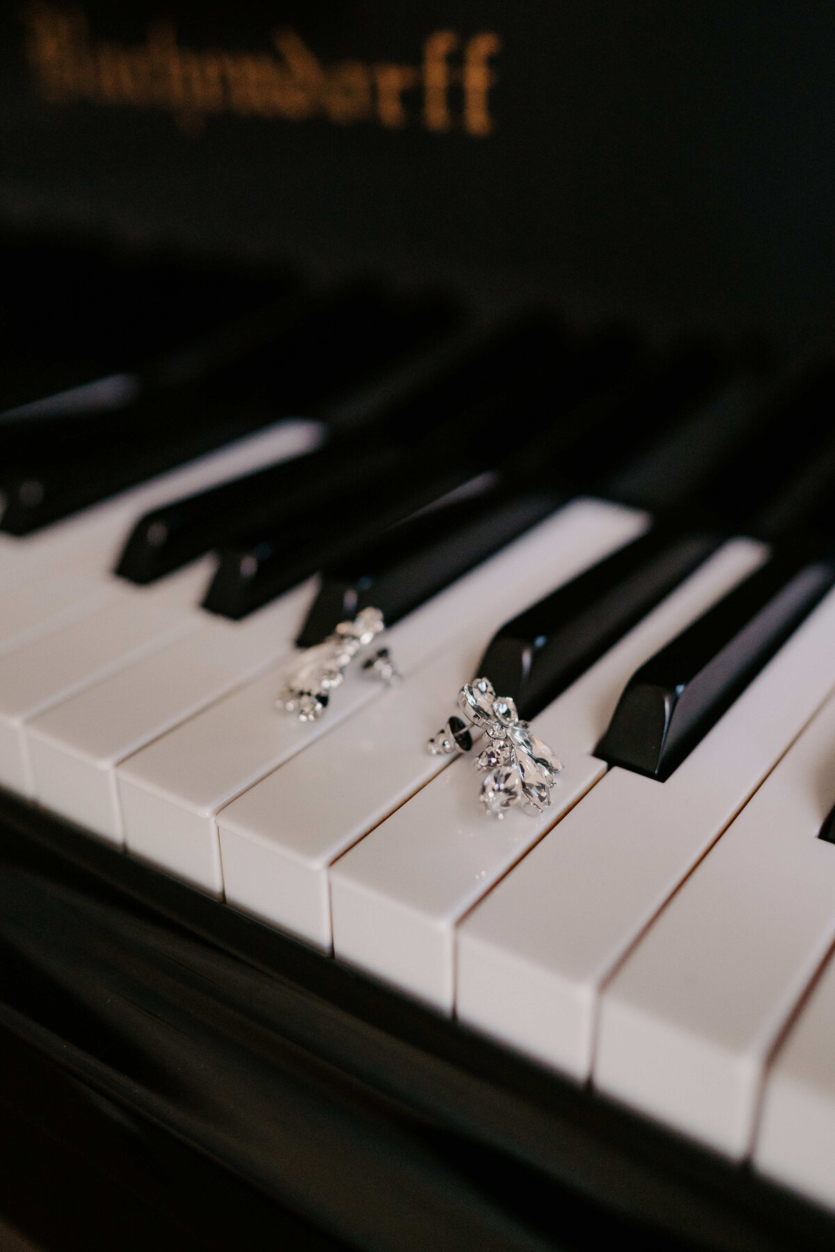 Two sparkling earrings rest on the black and white keys of a piano, creating a contrast of elegance and music, with a sense of harmony and sophistication.