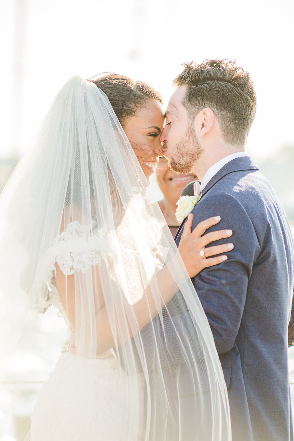 Close up image. A bride and groom are captured at The Bohlin in Newport, RI for candid wedding portraits. The bride and groom are in an embrace and the groom is kissing the bride's nose. Captured by Rhode Island Wedding Photographer Lia Rose Weddings