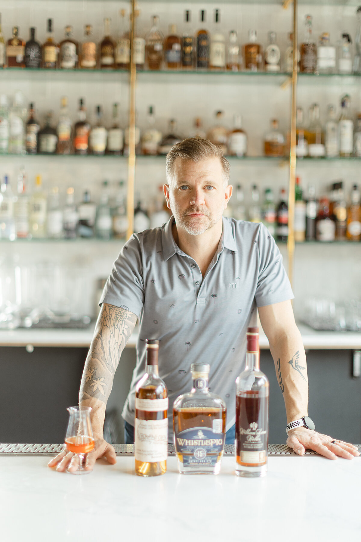 Professional headshot of a Dallas/Fort Worth business owner at his new restaurant Sip and Savor as he stands at the bar with bottles of alcohol in front of him.