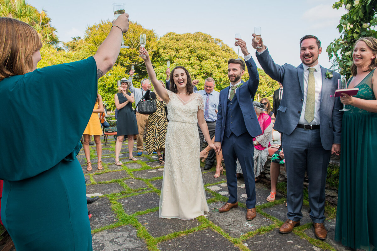 bride in vintage, beaded wedding dress with groom in blue suit toasting with their guests on the terrace of Westcove House, Kerry