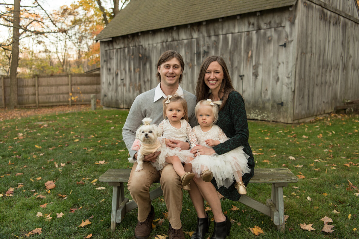 Family of four sitting on bench in front of barn in fall