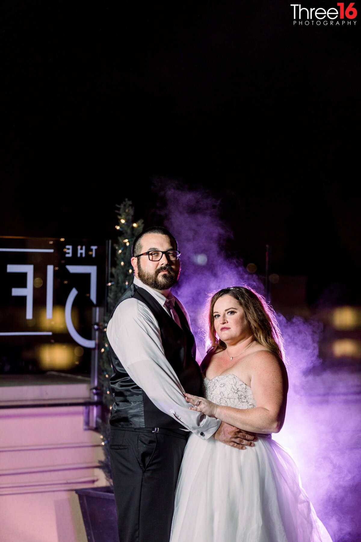 Newly married couple pose together under the evening sky with purple haze behind them