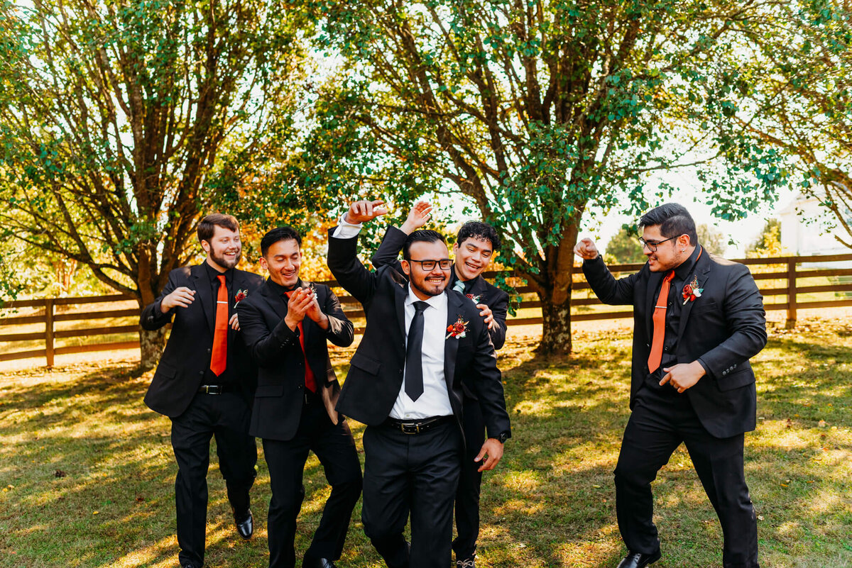 Photo of a groom and his groomsmen in black suits walking and cheering