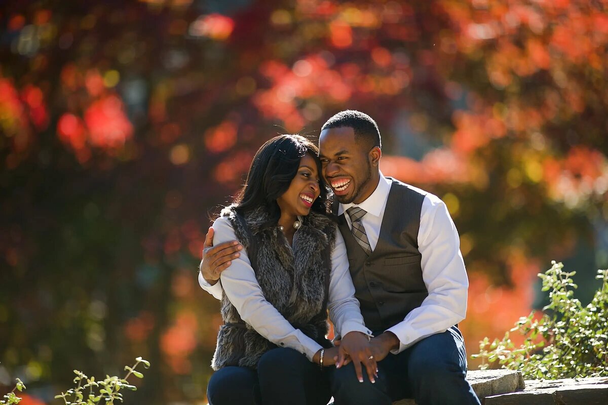 A couple sitting closely on a bench, surrounded by autumn leaves