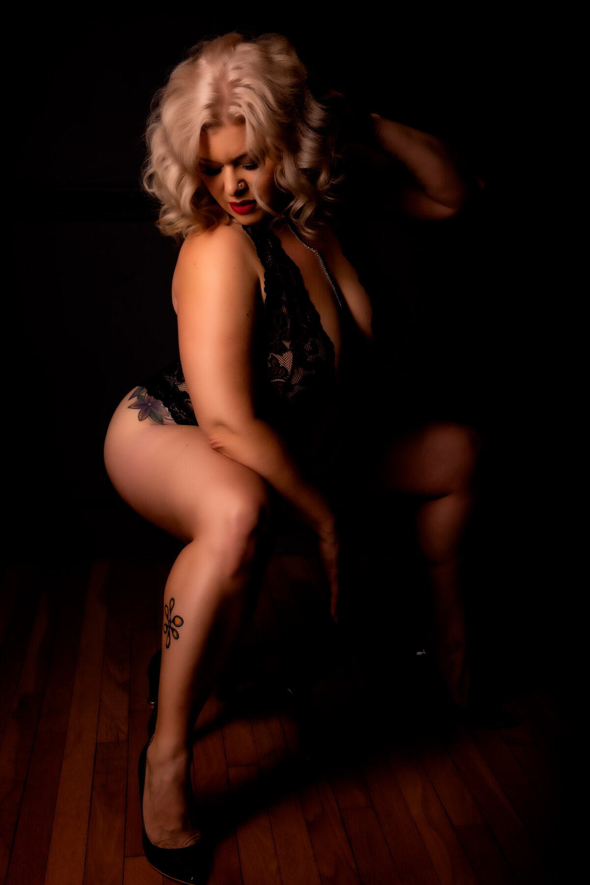 blonde hair woman sitting on a stool with her hand in her hair for her boudoir session