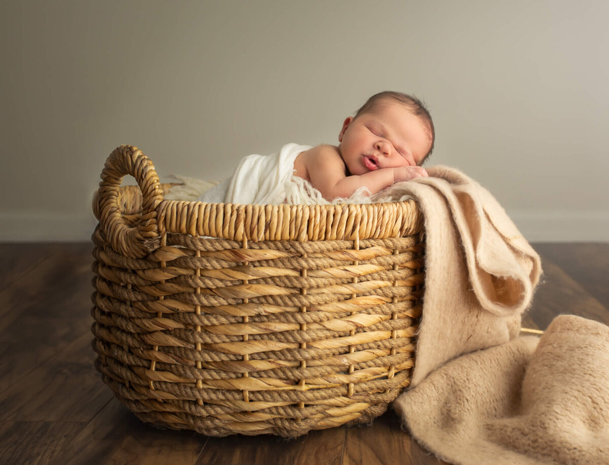 A newborn baby boy sleeps in a woven basket