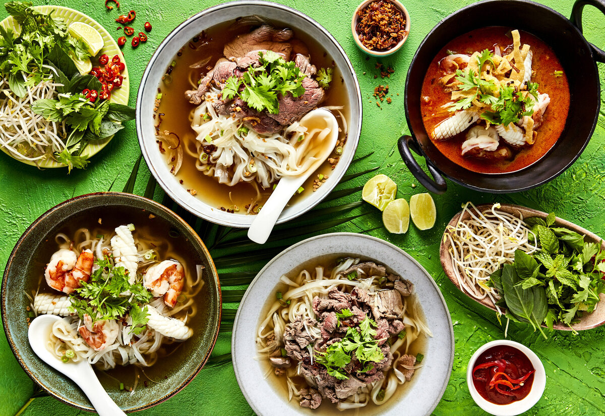 An overhead view of a table filled with various pho dishes and toppings to add to them.