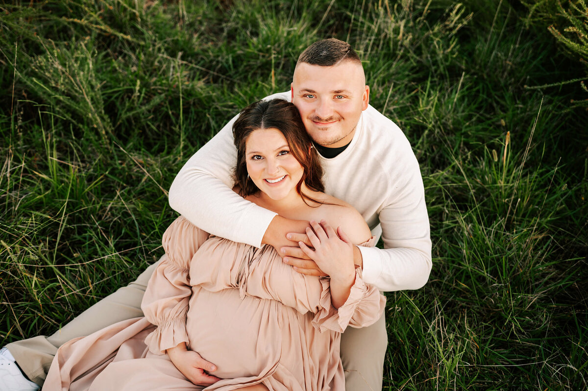 pregnant couple smiling sitting in grass captured by Springfield MO maternity photographer The XO Photography