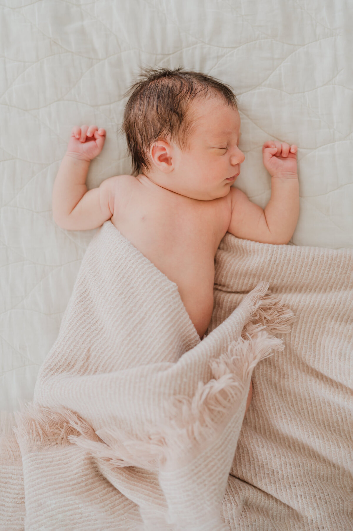 Overhead image of a sleeping baby wrapped in a pink blanket during lifestyle newborn photos.