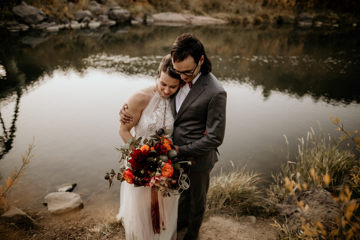bride leaning on groom in front of a river